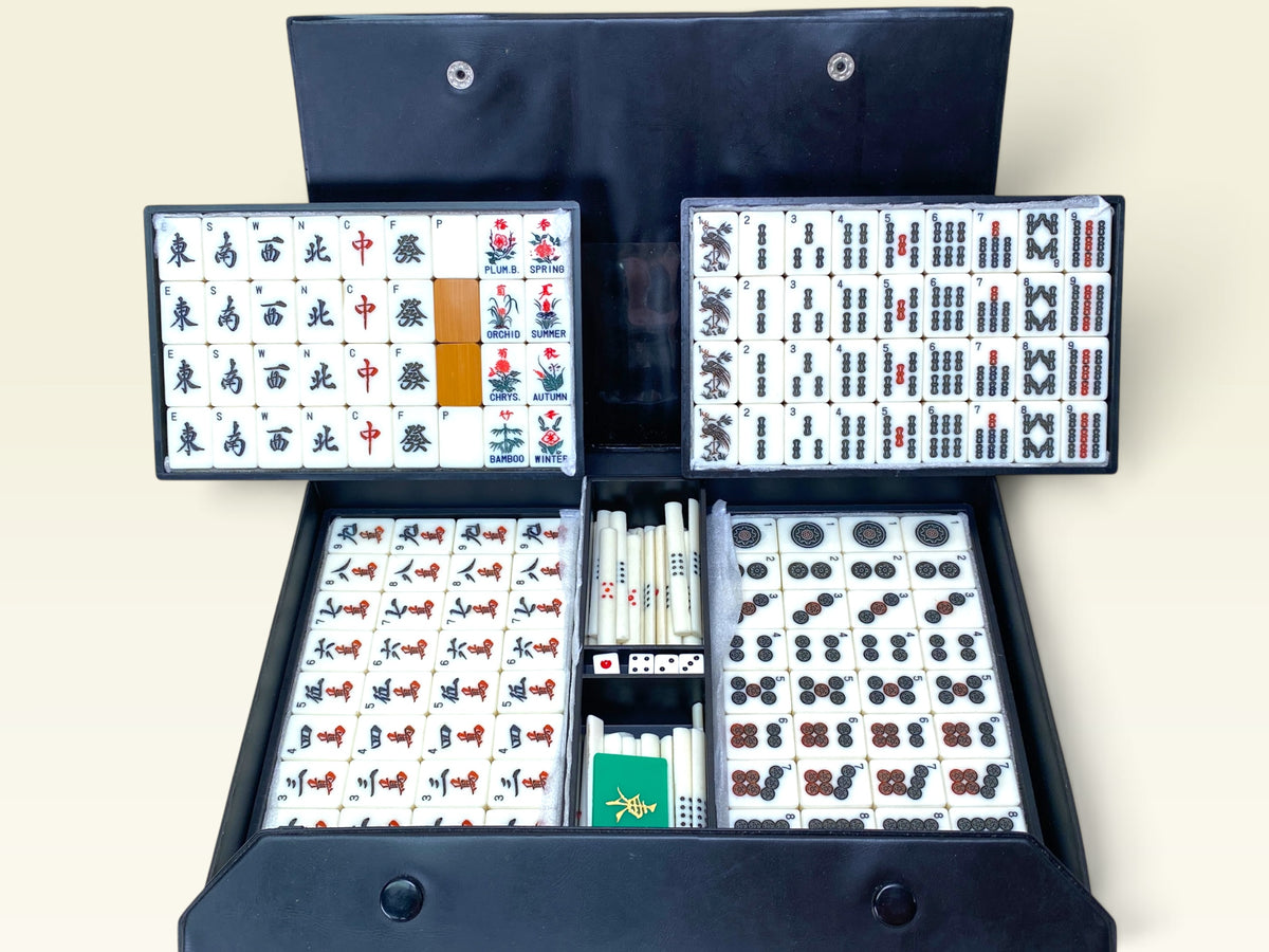 Open black portable case showing vintage Japanese mahjong tiles with bamboo backs, red chips, and white dice