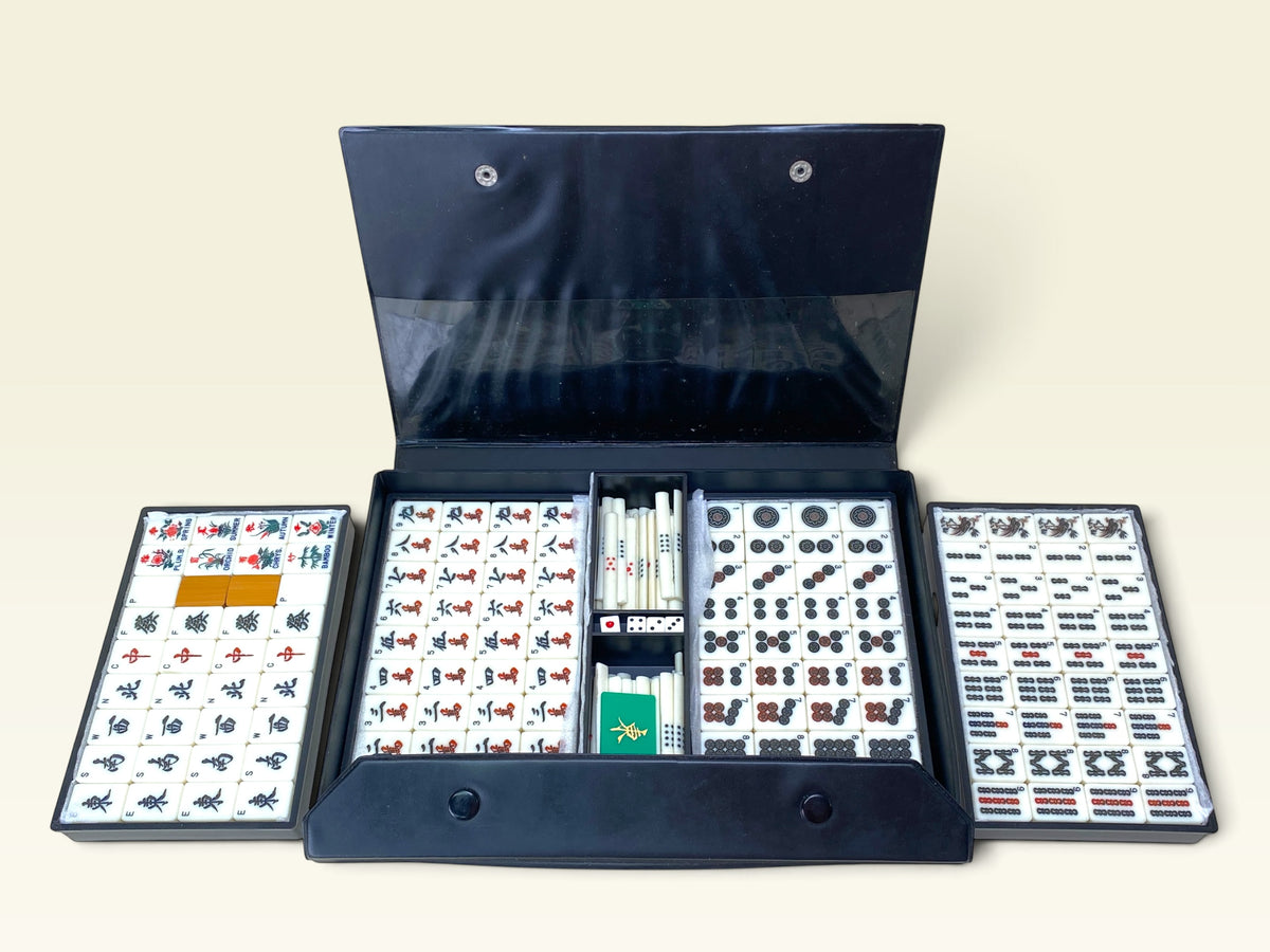 Vintage Japanese mahjong set with bamboo-back tiles arranged beside black portable carrying case