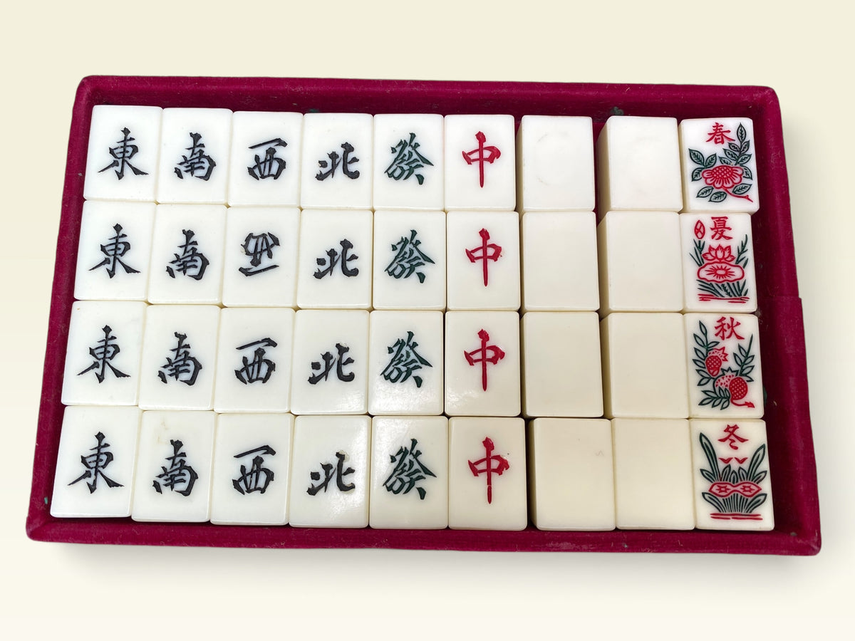 Mahjong wind and dragon tiles with visible bamboo backs in red velvet tray