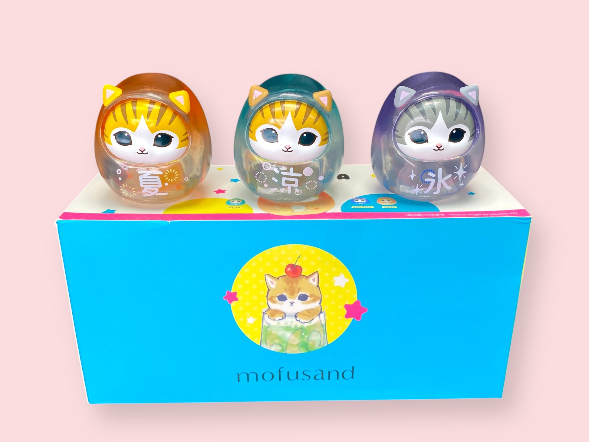 Three Mofusand Neko Soda Summer Transparent Daruma figures in their individual boxes, featuring orange, teal, and purple designs.